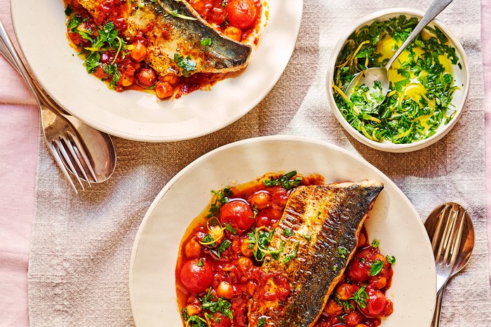 Two plates of mackerel with crisp skin sat on a tomato and chickpea mix with a pink linen background