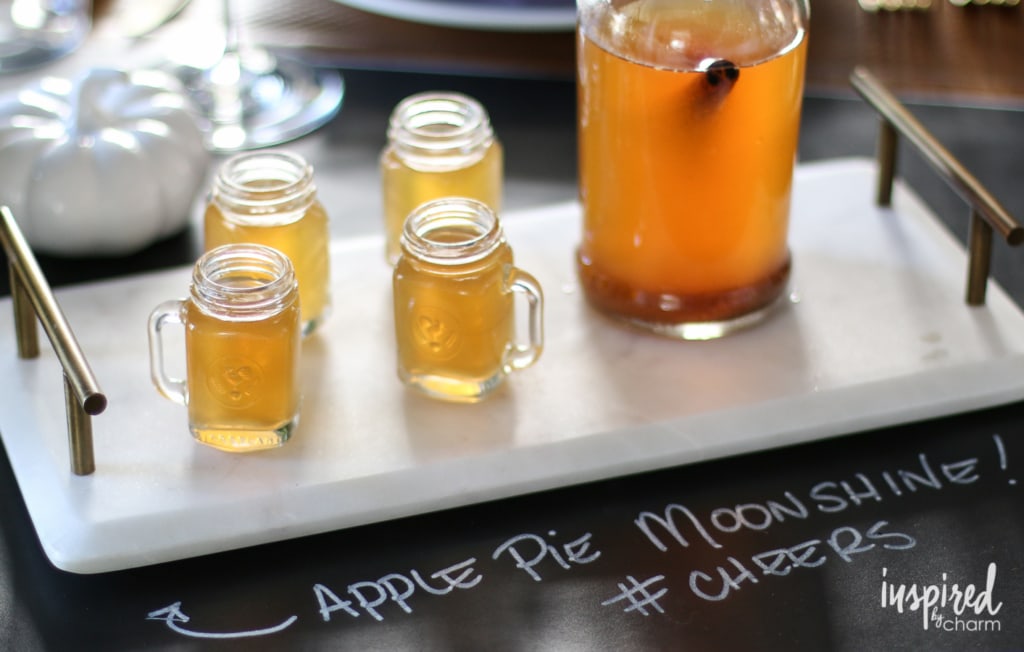 4 shot glasses next to a container of apple pie moonshine
