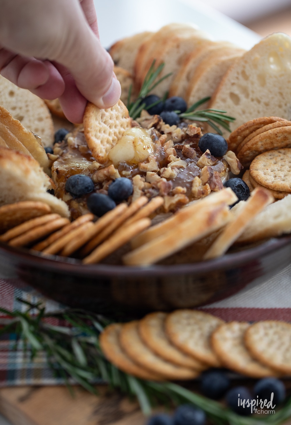 hand with cracker scooping a bit of baked brie with jam on it.