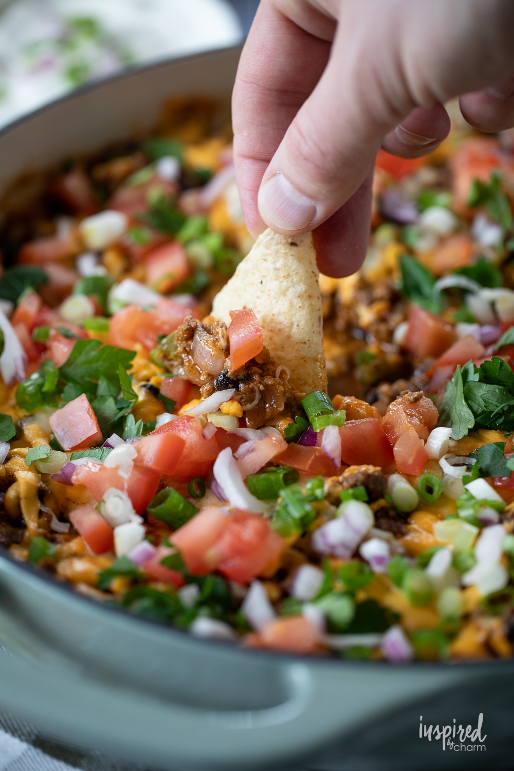 hand with a chip taking a scoop of hot taco dip.
