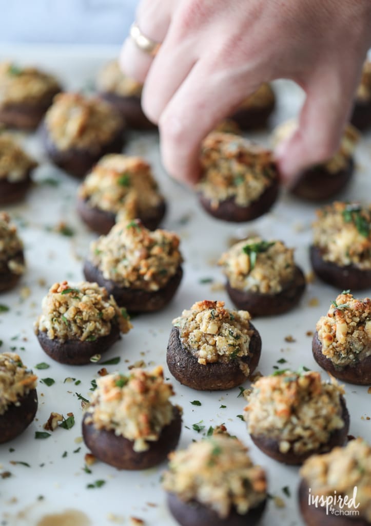 hand taking a Walnut and Blue Cheese-Stuffed Mushroom from a serving dish fill of them.