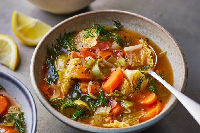 Bowl of cabbage broth with a spoon sticking out next to lemon wedges