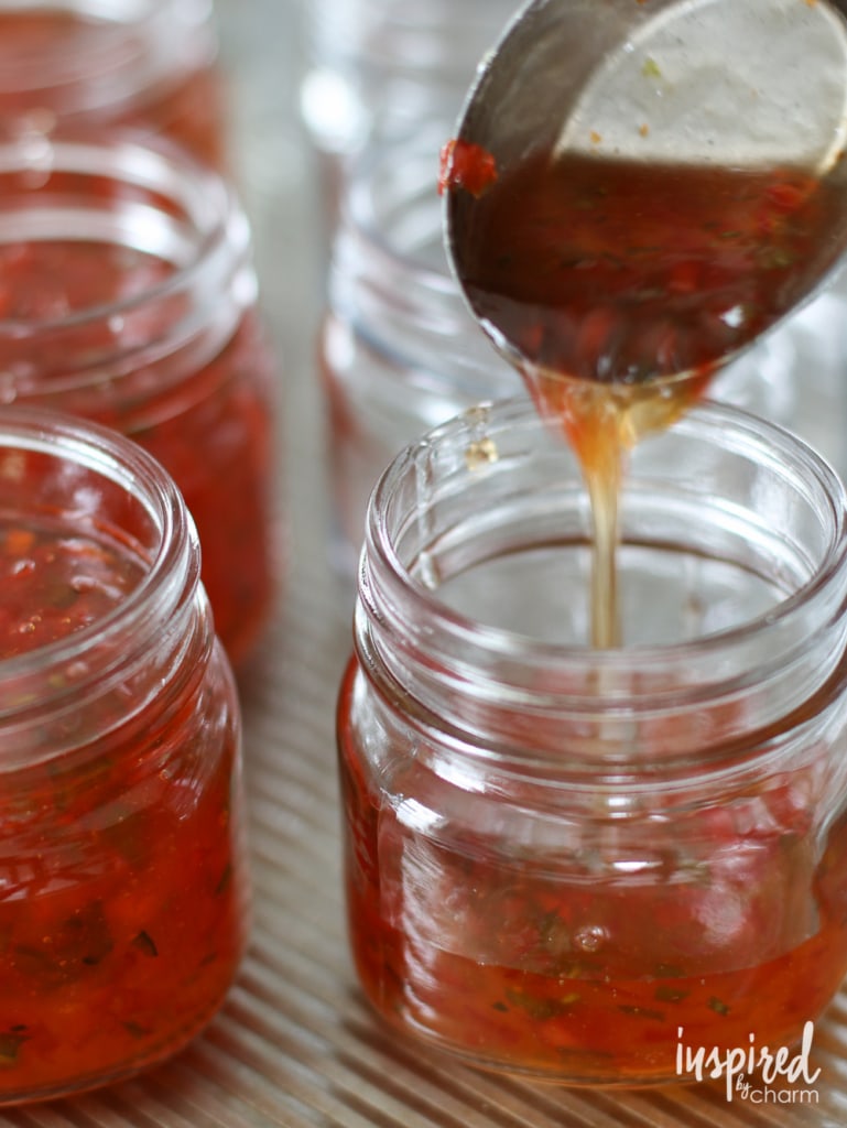 red pepper jelly pouring off of a spoon into a small jar