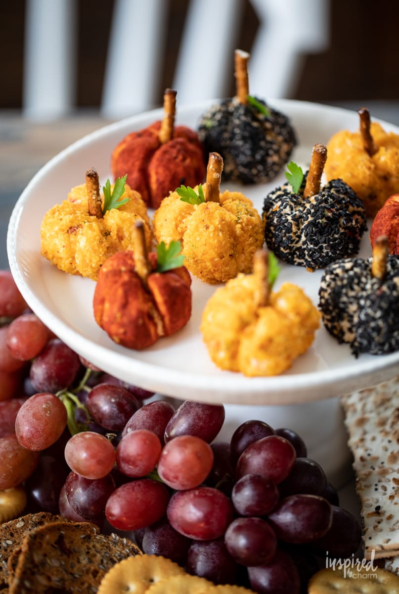 small white cake stand with Mini Pumpkin Cheese Balls, grapes, and crackers.