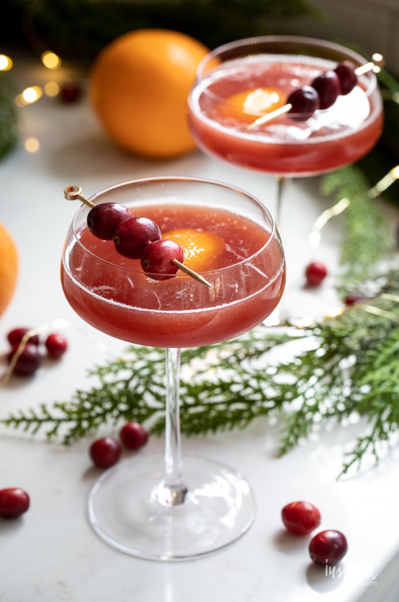Cranberry Manhattan in a tall glass with cranberry and orange garnish.