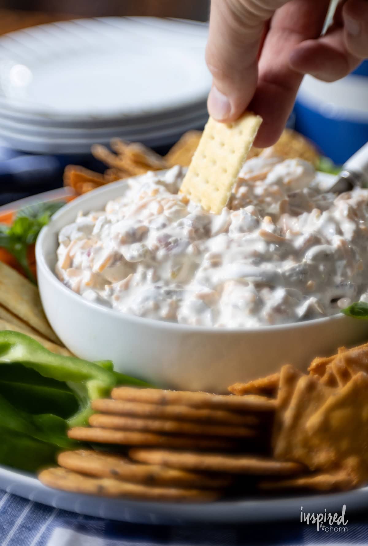 hand with a cracker dipping into Creamy Jalapeño Bacon Dip.