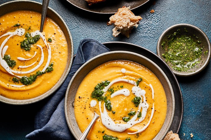 Two bowls of curried swede soup topped with coconut milk and coriander next to a plate with ripped crusty bread