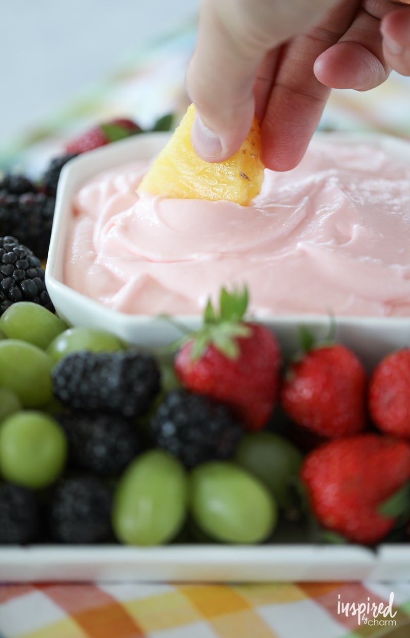 hand holding a piece of pineapple scooping fruit dip. 