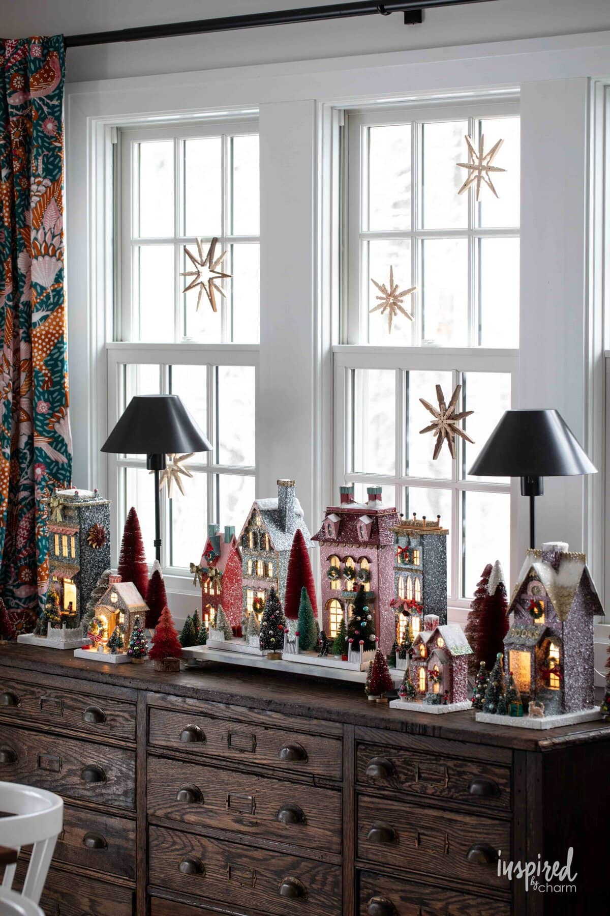 Christmas houses on a sideboard with Clothespin Snowflakes hung above them.