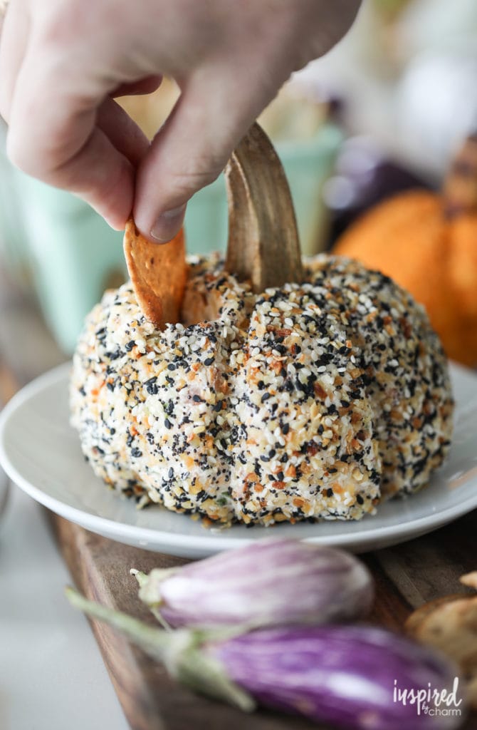 hand putting a round cracker into an everything bagel cheese ball shaped like a pumpkin.