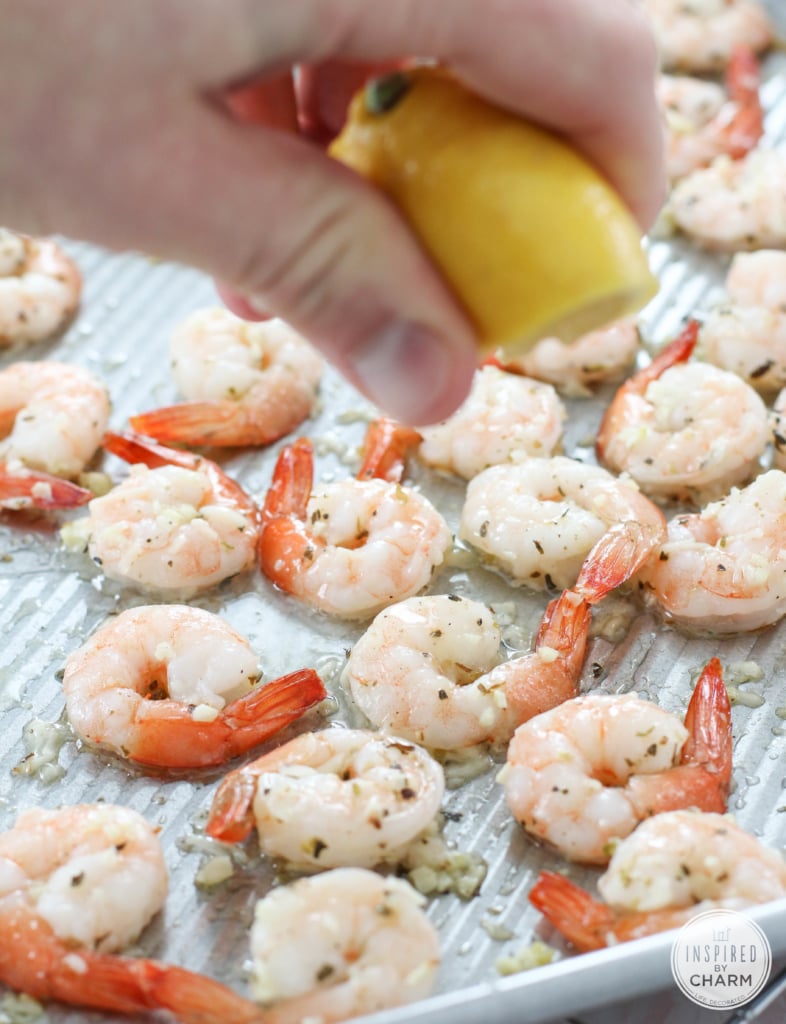 hand squeezing lemon over Roasted Parmesan Garlic Shrimp on a baking pan.
