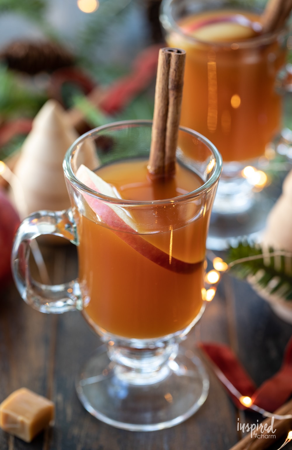 clear glass of spiked caramel apple cider tea in a glass with a cinnamon stick.