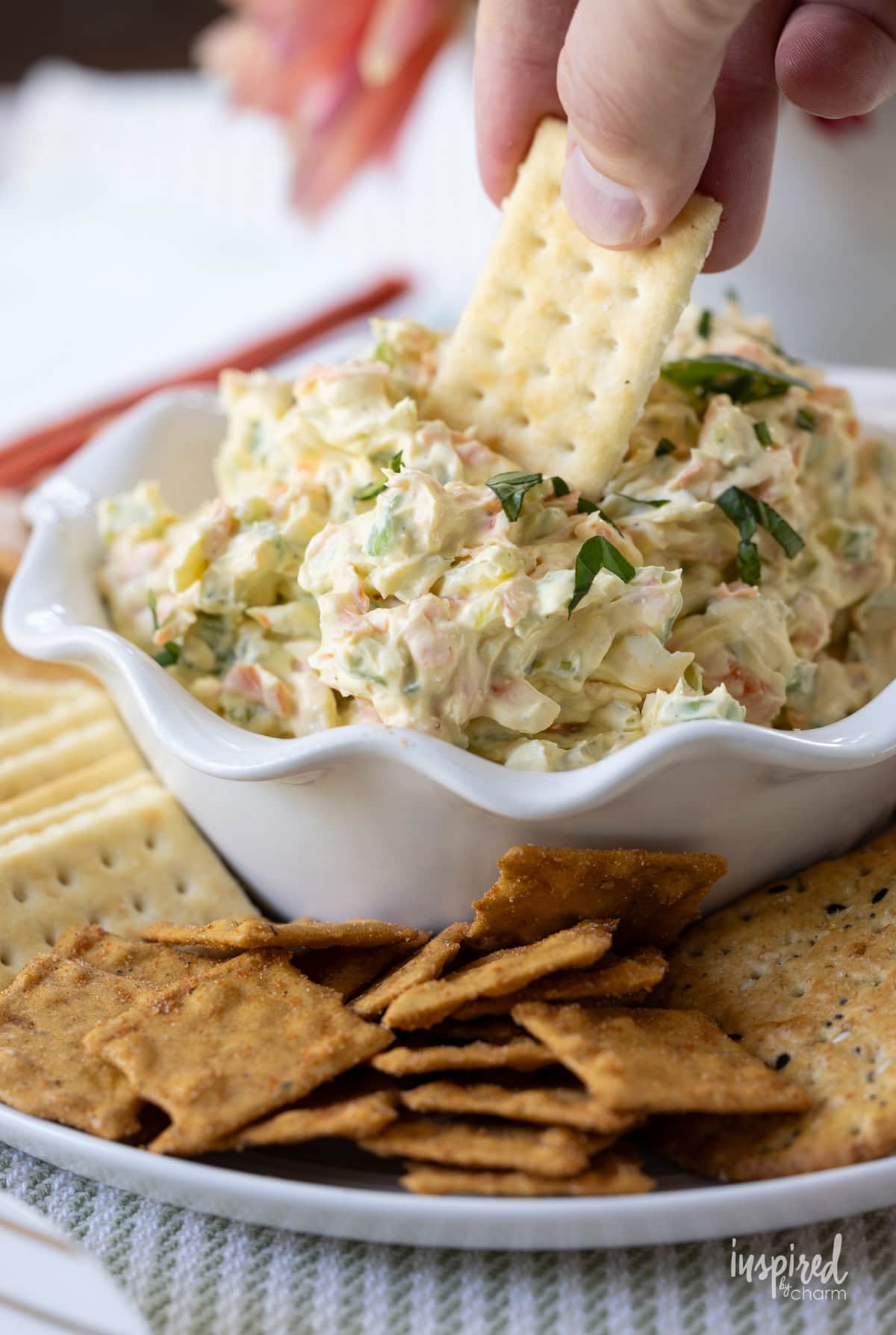 hand dipping a cracker into creamy vegetable dip.