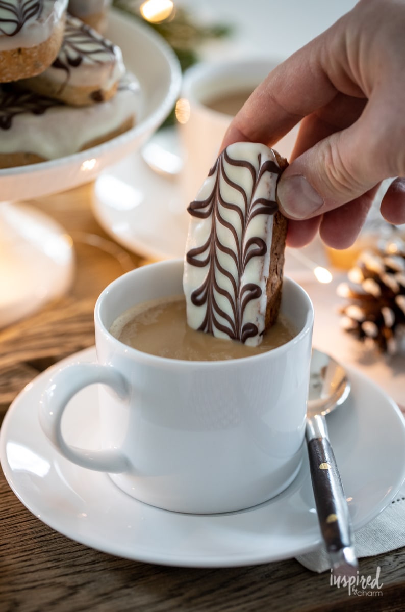 hand dunking Almond and Hazelnut Biscotti in coffee.