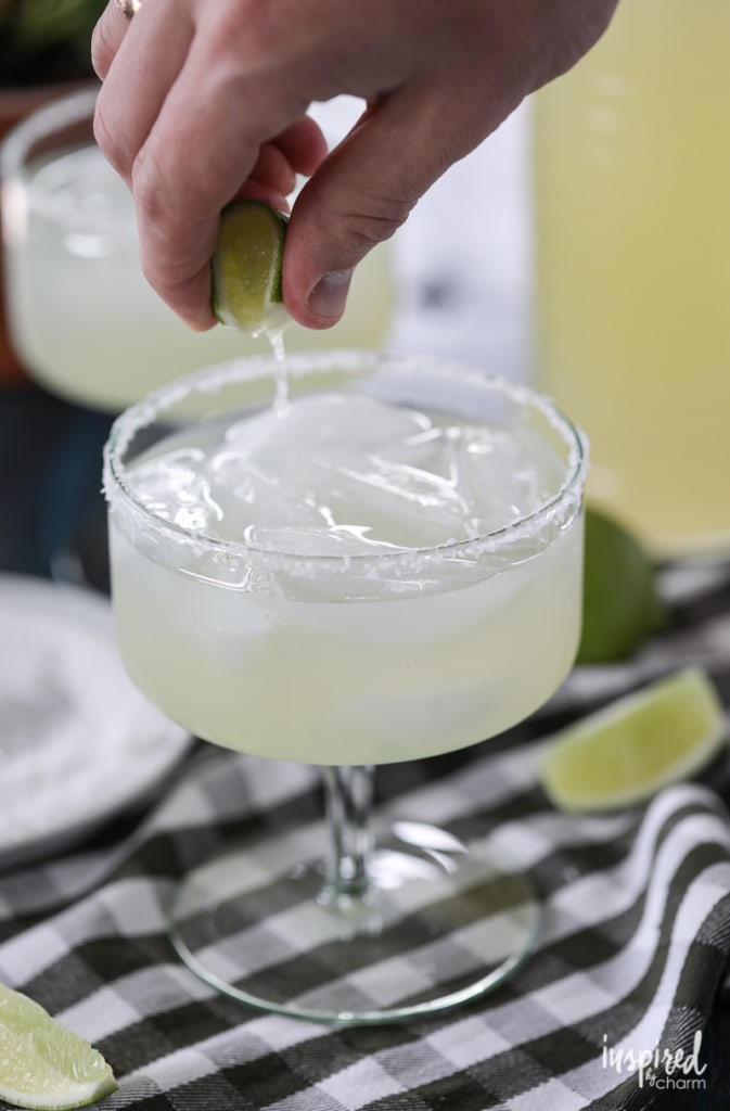 hand with a lime squeezing into a margarita.