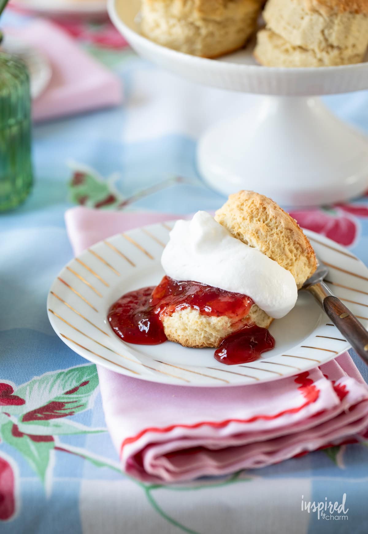 single scone cut in half filled with strawberry jam and whipped cream.