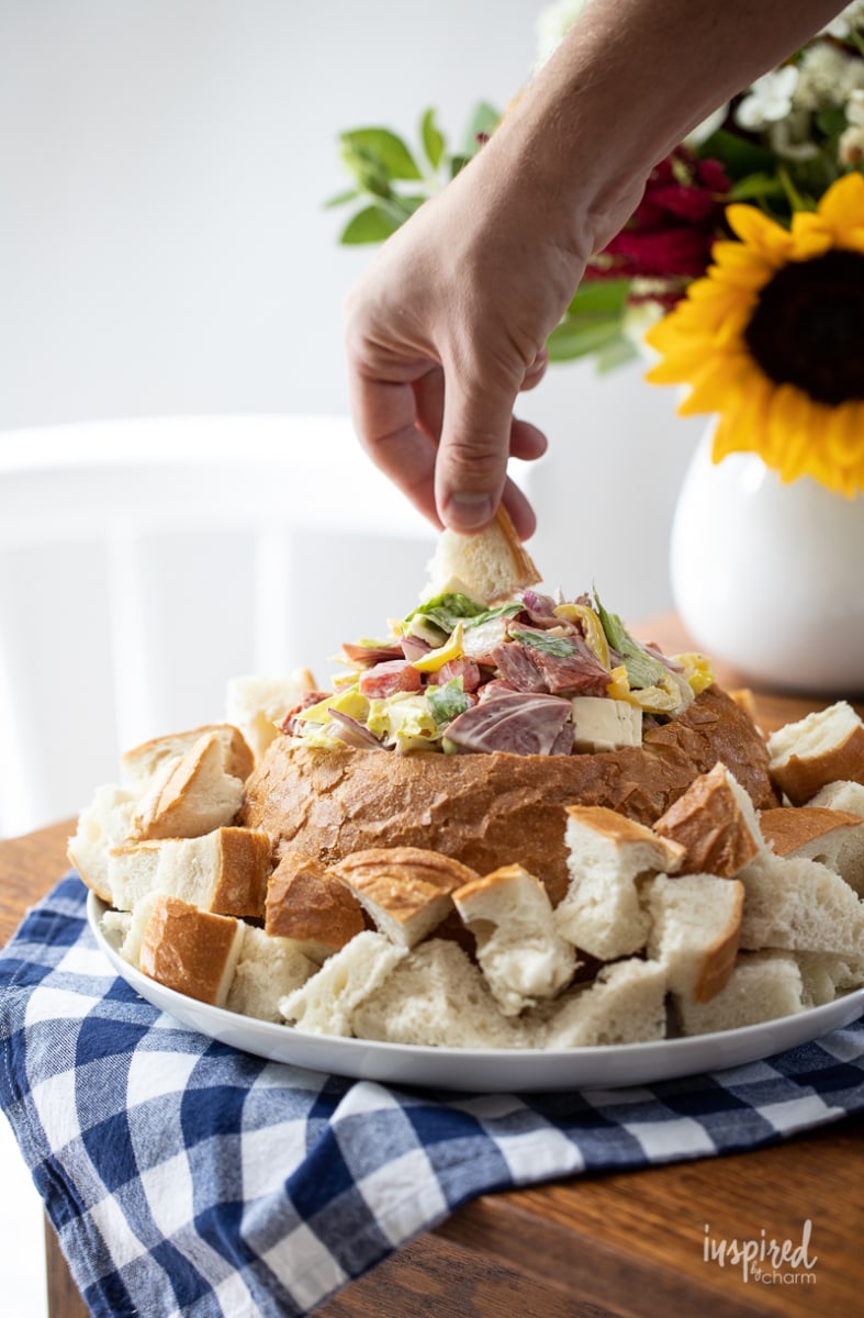 hand dipping into Italian hoagie dip in bread bowl.