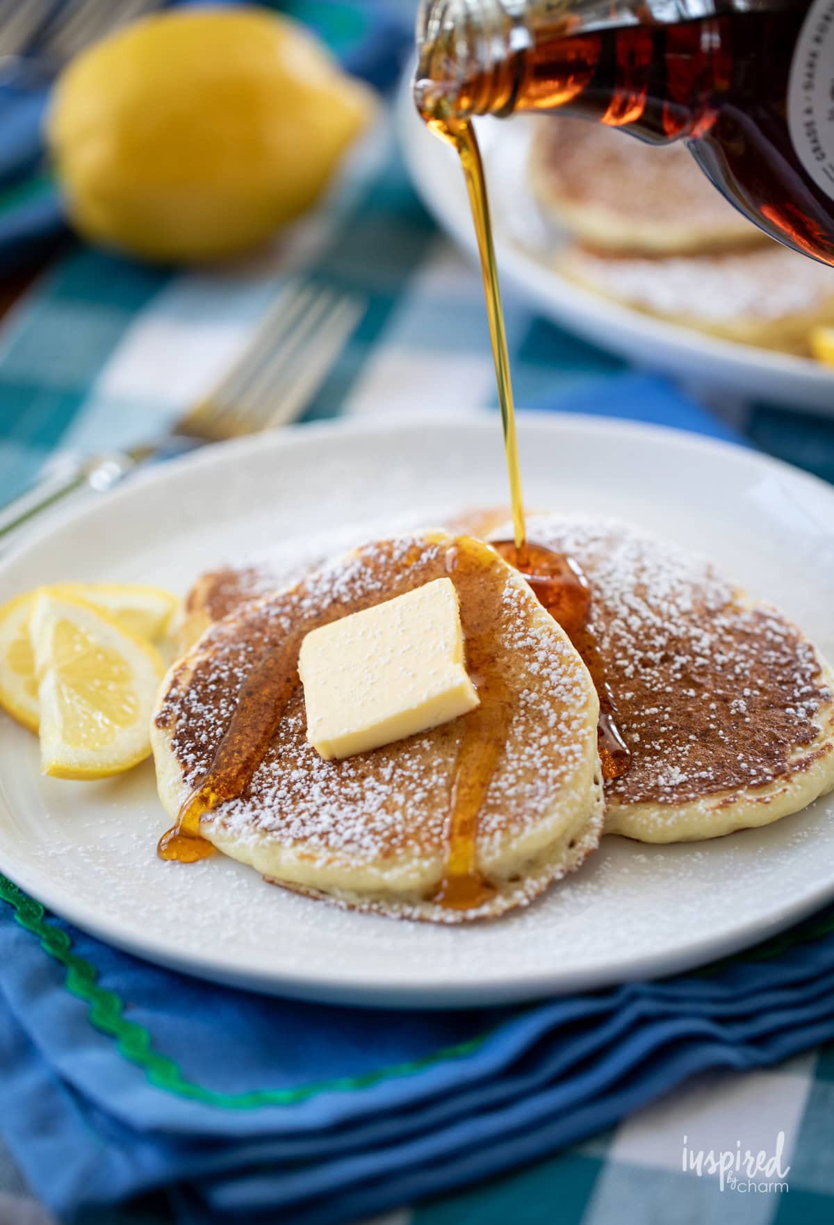 bottle of maple syrup being poured over lemon ricotta pancakes.