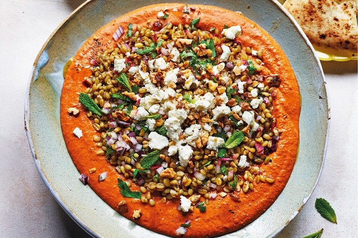 a plate of red muhammara sauce topped with grains and herbs