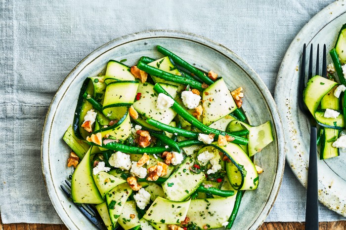 A green courgette salad on a grey plate and light blue background