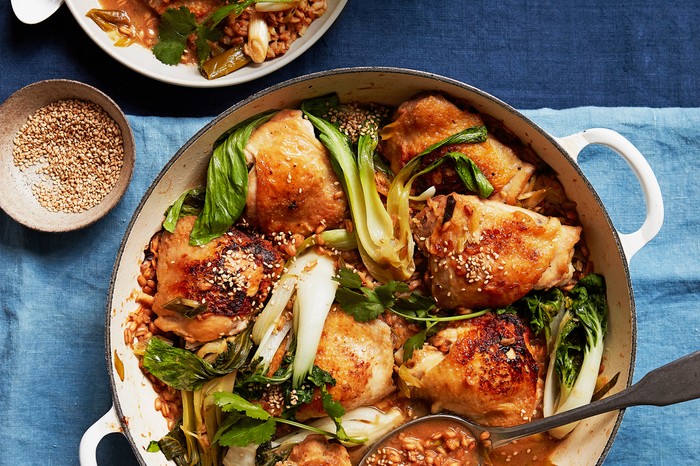 A white casserole dish filled with crispy chicken thighs and green pak choi