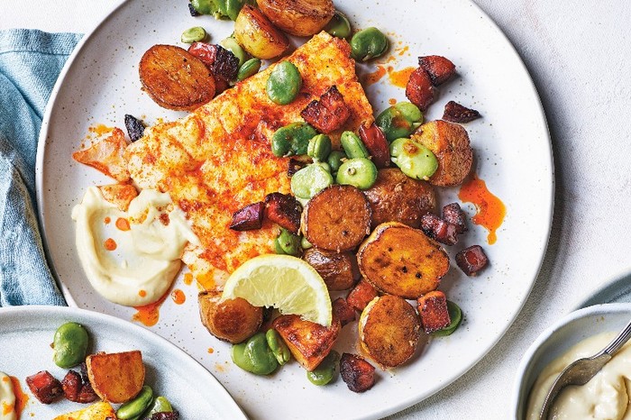 a white plate filled with crisp, golden new potatoes, paprika-coated hake and green broad beans