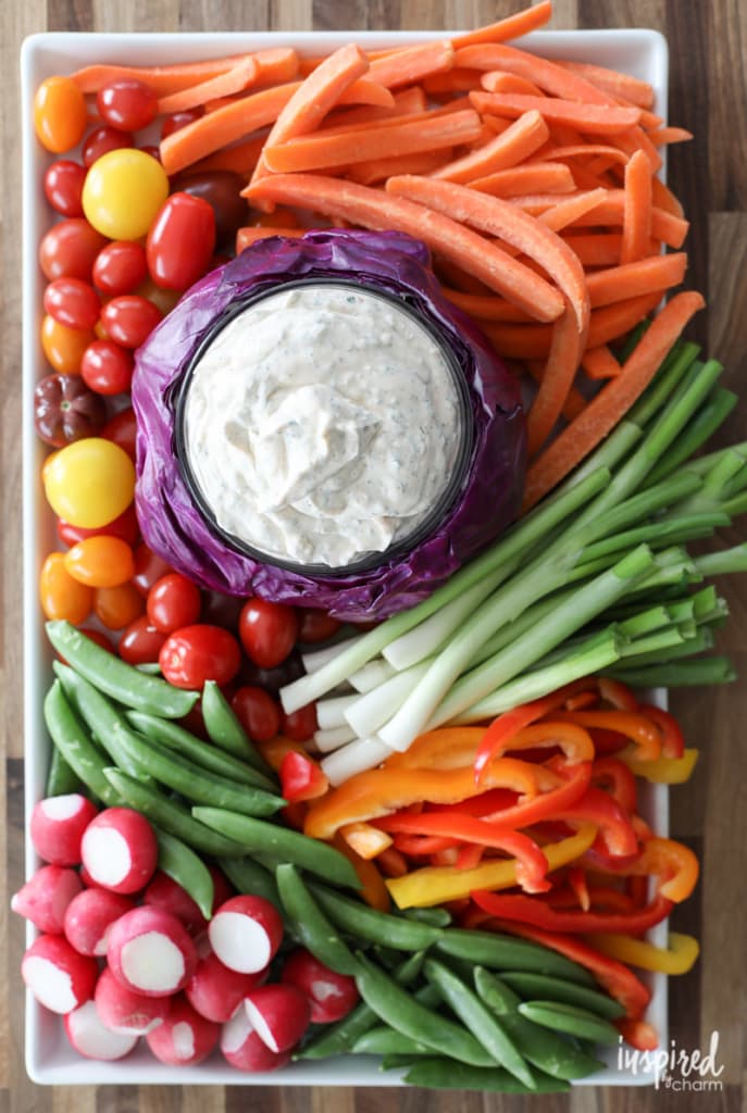 Vegetable dip in a cabbage bowl surrounded by cut vegetables.
