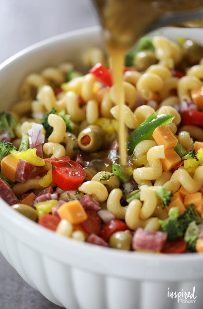 adding dressing to really good pasta salad in a large white bowl.