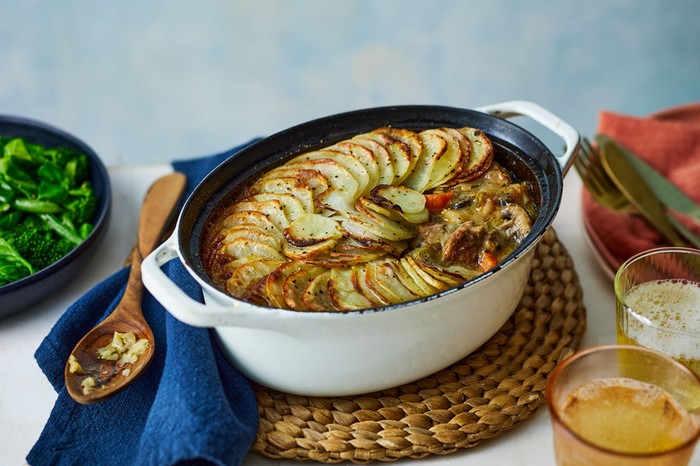 Pot of pork stew topped with sliced potatoes with a wooden spoon lying next to it