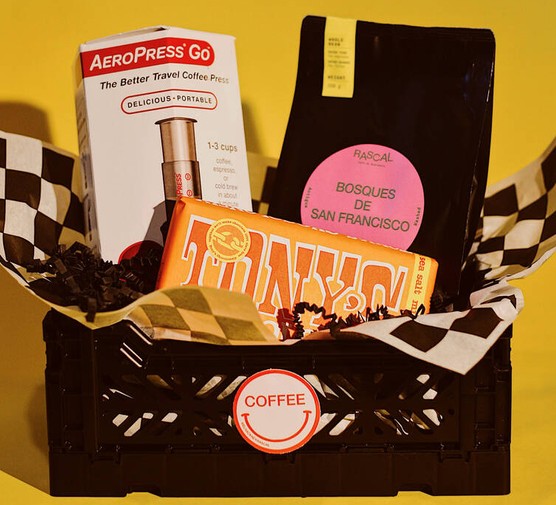 A black crate containing a bar of Tony's chocolate, a bag of coffee and an aeropress