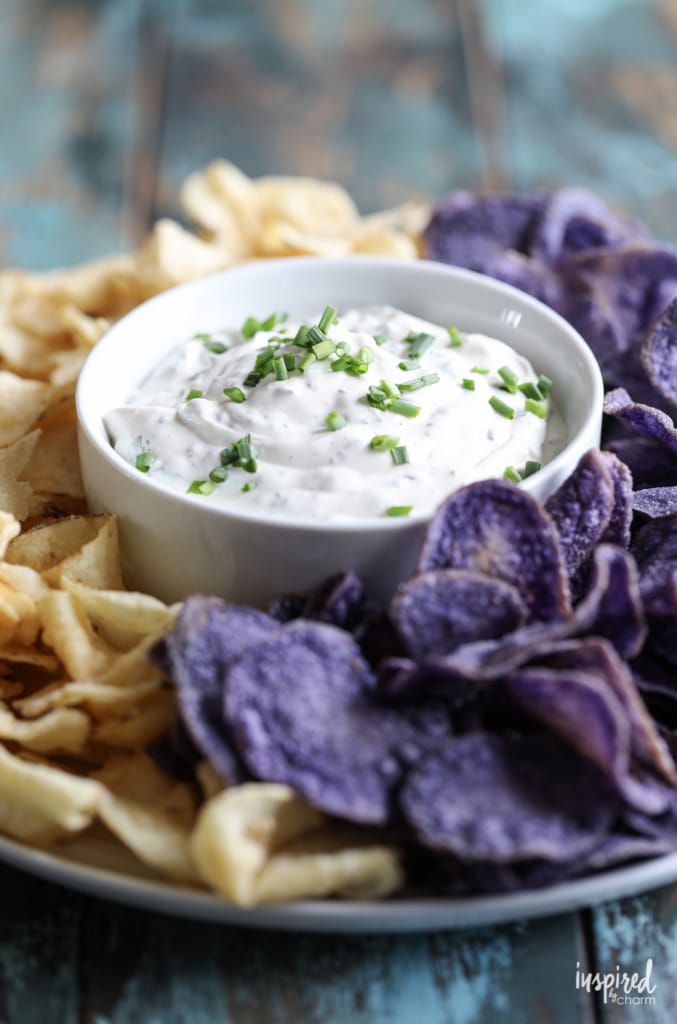 chip dip in a bowl surrounded by potato chips on a plate.