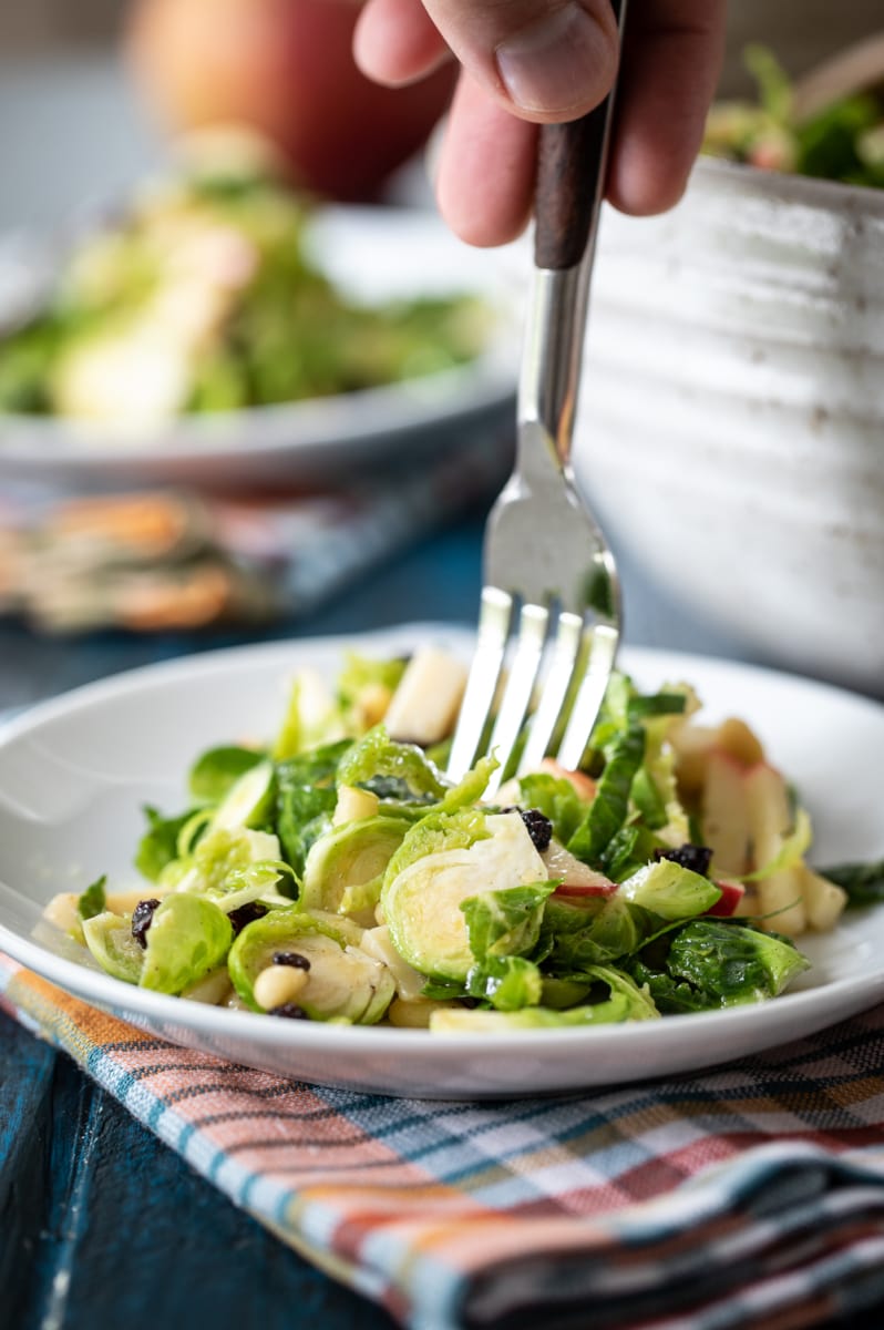 hand with fork taking a bite form Shaved Brussels Sprout Salad.