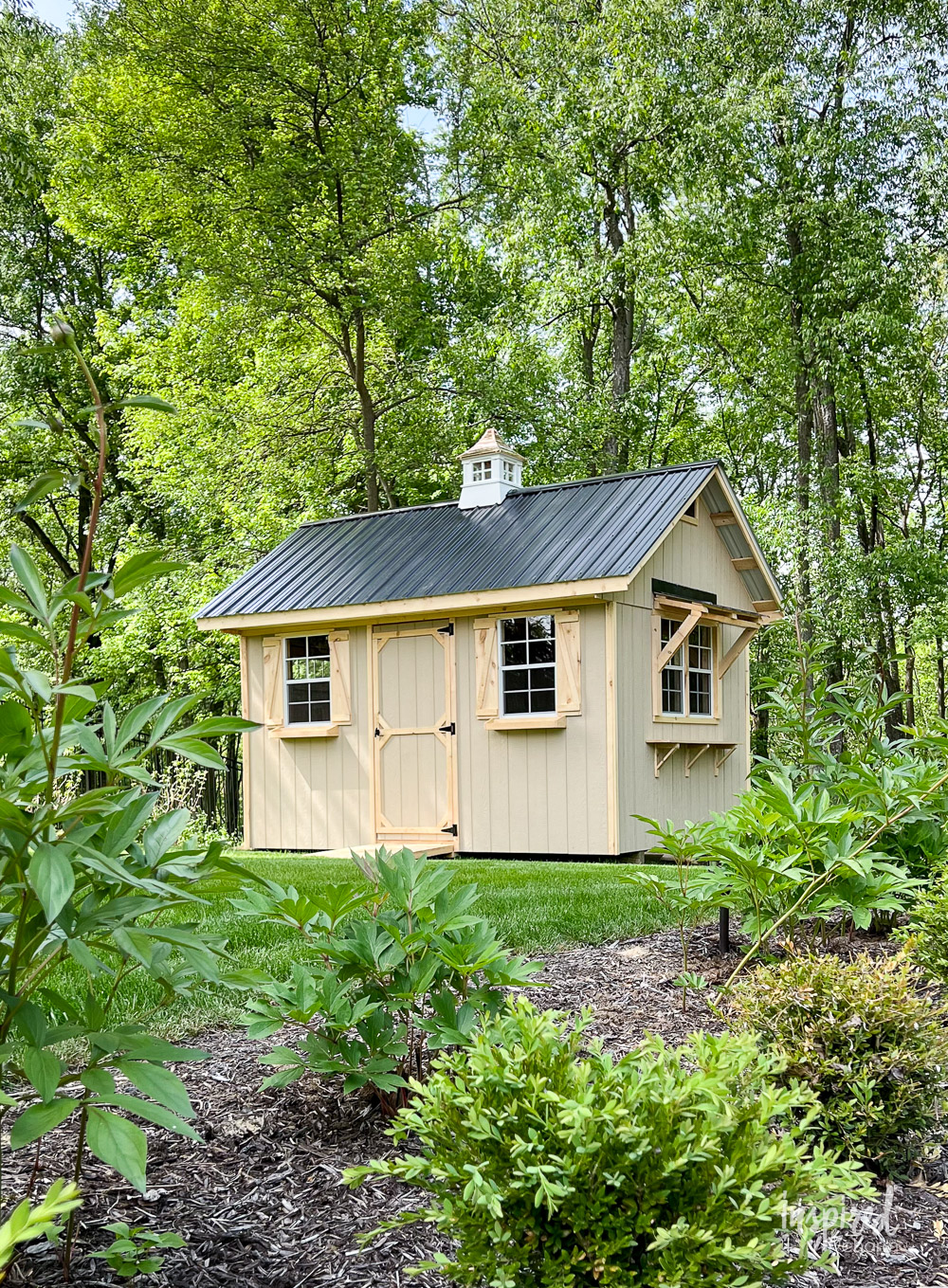 wood shed in a backyard surrounded by trees.