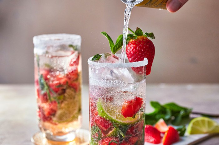 Two glasses of strawberry mojitos and fruit, hand pouring tonic water