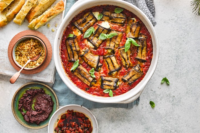 A big serving bowl full of tomato sauce with stuffed aubergine rolls on top and basil for decoration