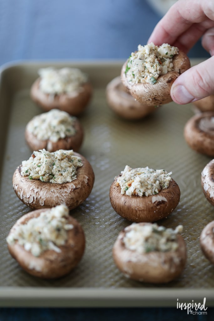 hand adding a Walnut and Blue Cheese-Stuffed Mushroom to a baking sheet.