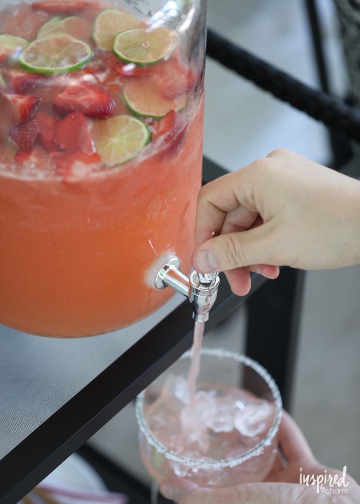 hand filling a glass with Strawberry Margarita Punch from a beverage dispenser. 