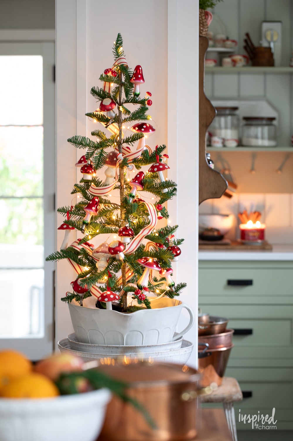 adorable mini christmas tree in a bowl decorated with ribbon, lights, and mushroom ornaments.