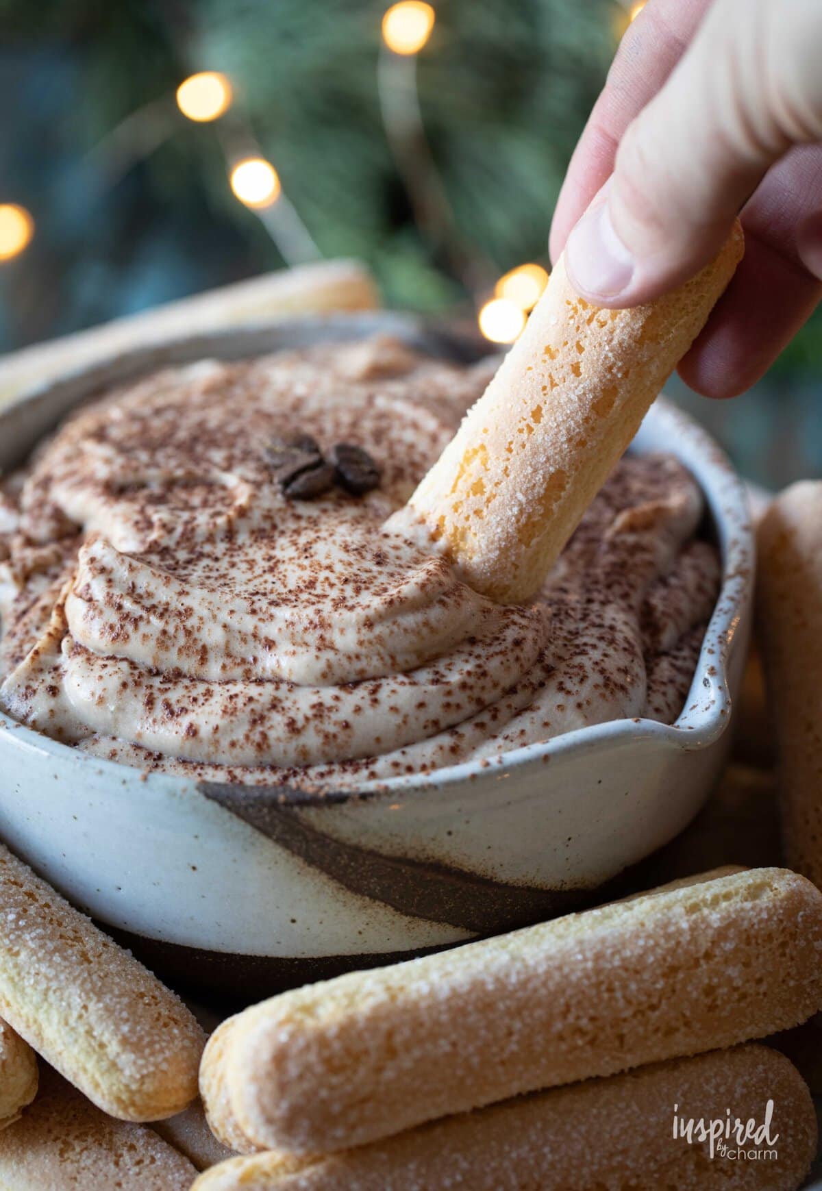 hand with ladyfinger dipping into tiramisu dip.
