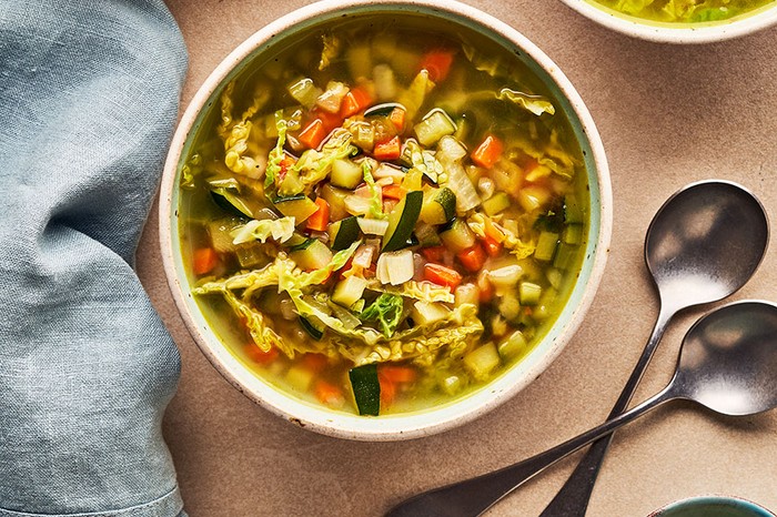 Bowl of vegetable soup next to two slices of bread and a ramekin of lemon zest