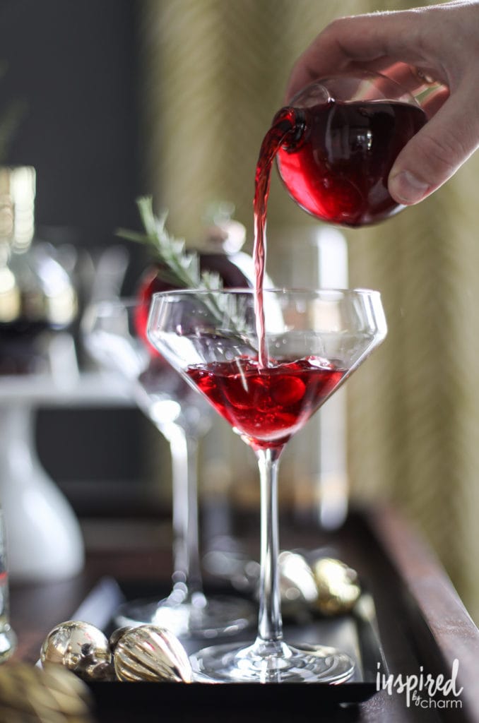 a clear ornament filled with cocktail, pouring into a tall glass