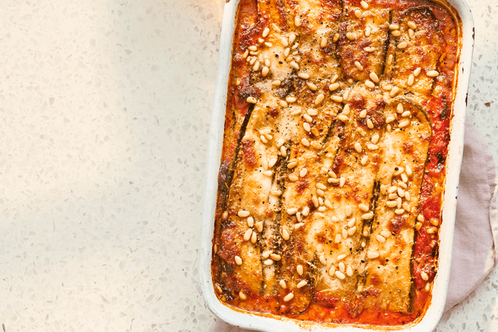 Baking dish with courgette parmigiana topped with toasted pine nuts