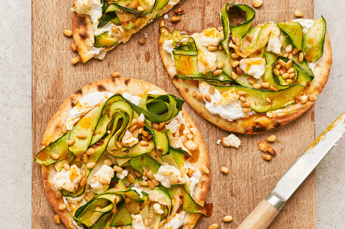 Flatbreads on a wooden board topped with shavings of courgette