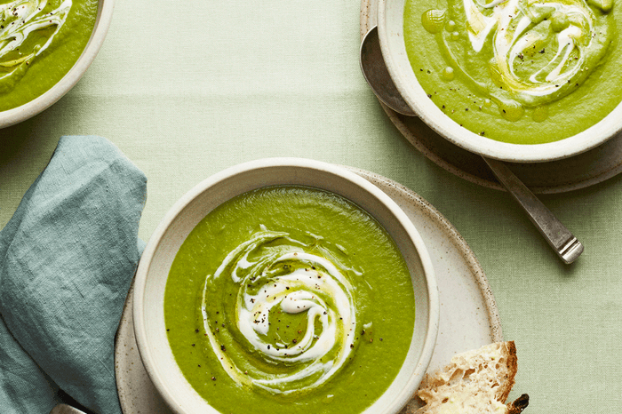 Bowls of green wild green soup topped with a swirl of crème fraîche